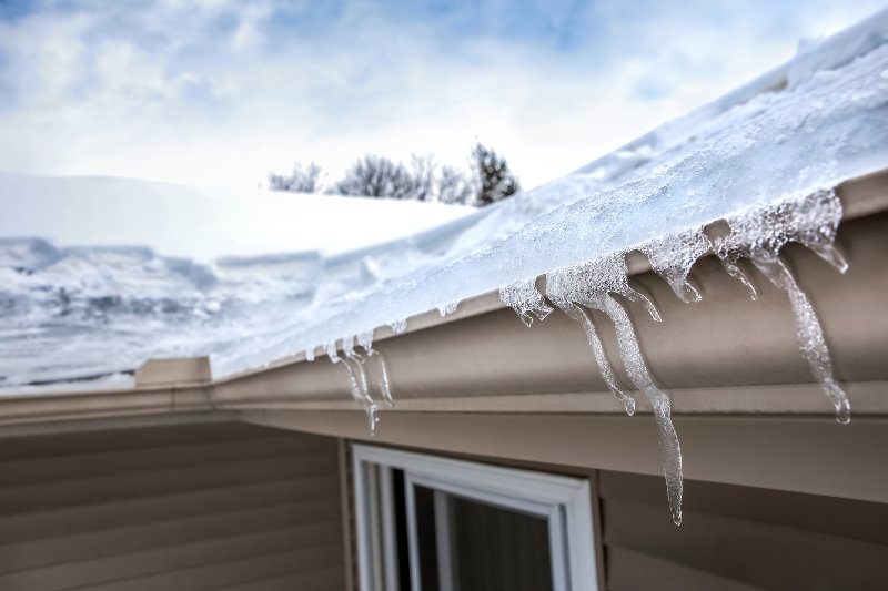 Ice dam in gutter and ice frozen on roof in winter, shallow focus on icicles in foreground