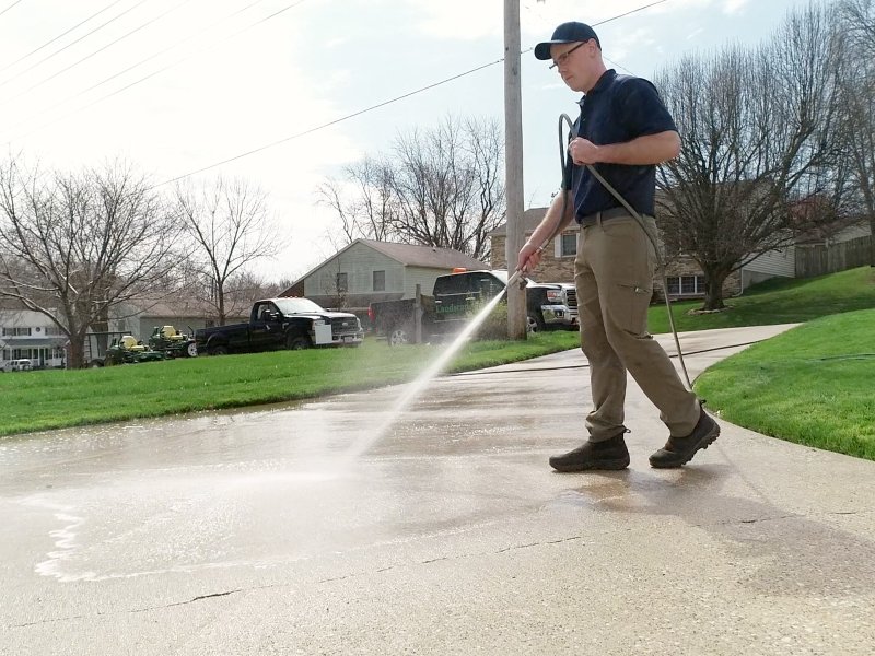 Pressure washing a driveway with a power washer machine spraying water and removing dirt and grime